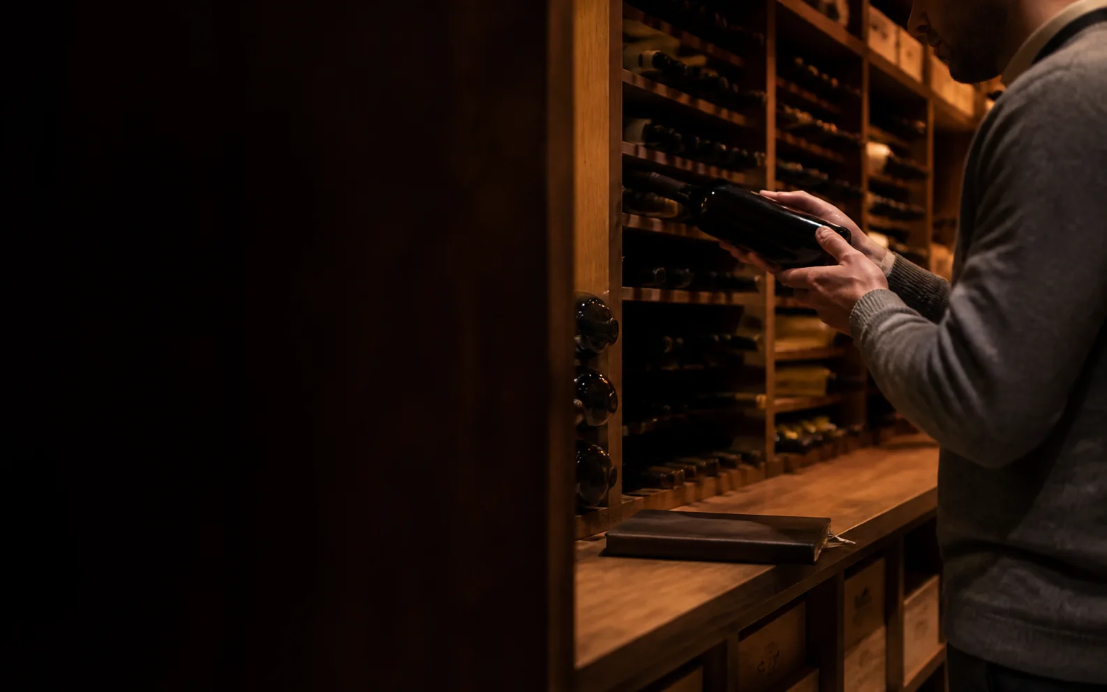 A collector organising unbranded bottles in a warm timber cellar